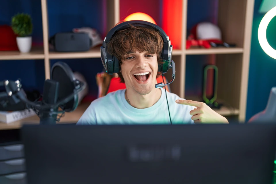 Uśmiechnięty streamer w słuchawkach z mikrofonem przed laptopem w gamingowym pokoju