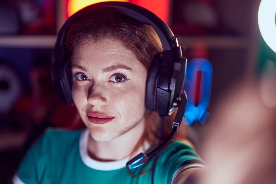 Uśmiechnięta streamerka w słuchawkach z mikrofonem w kolorowym oświetleniu gamingowym